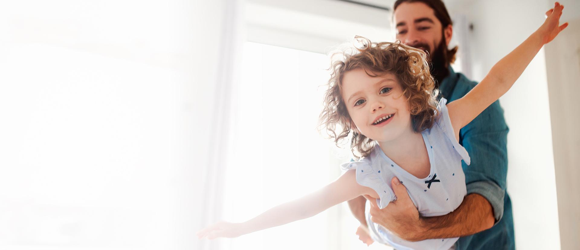 Ein Vater hält ein junges Mädchen in den Armen, das Flugzeug spielt.